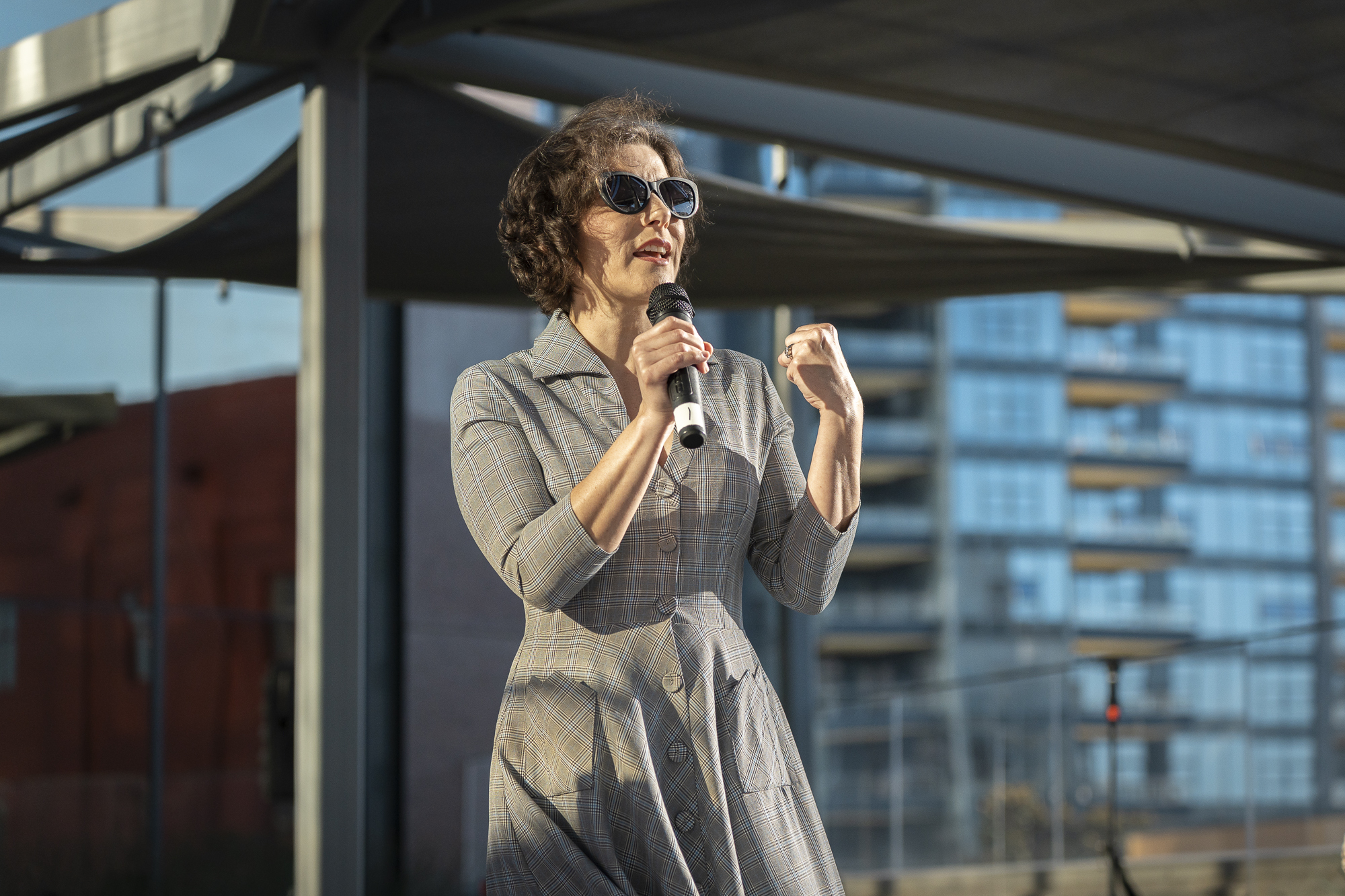 A woman wearing sunglasses speaks into a microphone.