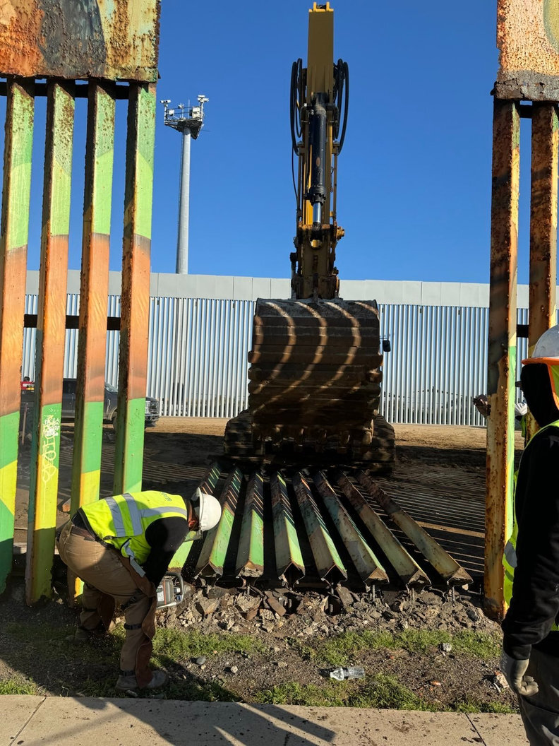 A construction worker taking down a border wall piece