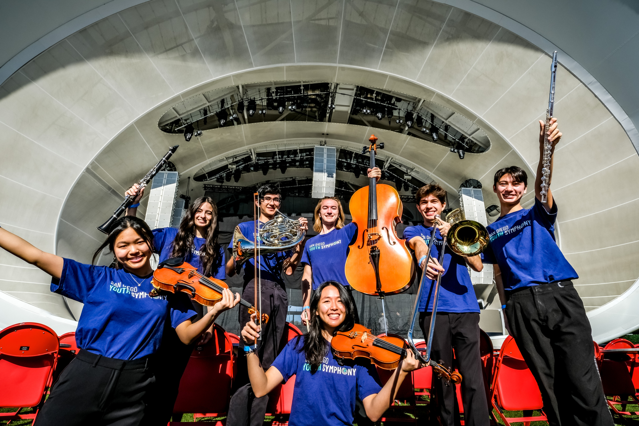 Smiling students holding their orchestra instruments up in front of Rady Shell